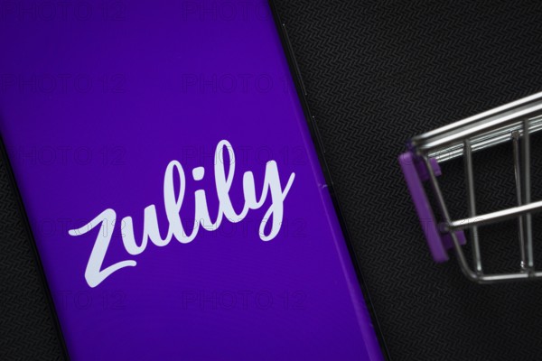 Dhaka, Bangladesh- 03 July 2025: A smartphone displaying the Zulily logo next to a miniature shopping cart on a background