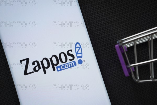 Dhaka, Bangladesh- 03 July 2025: A smartphone displaying the Zappos logo next to a miniature shopping cart on a background