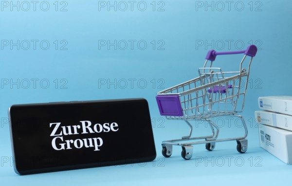 Dhaka, Bangladesh- 03 July 2025: Smartphone with Zur Rose Group logo next to a small shopping cart and boxes against a blue background