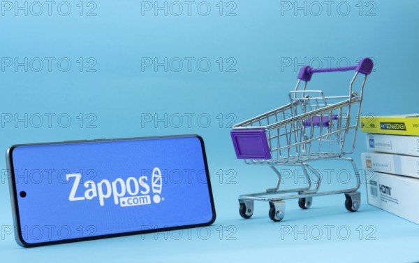 Dhaka, Bangladesh- 03 July 2025: Smartphone with Zappos logo next to a small shopping cart and boxes against a blue background