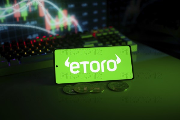 EToro logo on phone with coins and stock chart backdrop, evoking digital trading atmosphere