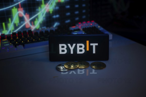 BYBIT logo on smartphone, accompanied by coins and stock chart, conveying trading theme
