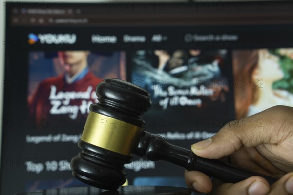 Dhaka, Bangladesh- 20 June 2025: A hand holds a gavel in front of a computer screen displaying YOUKU website
