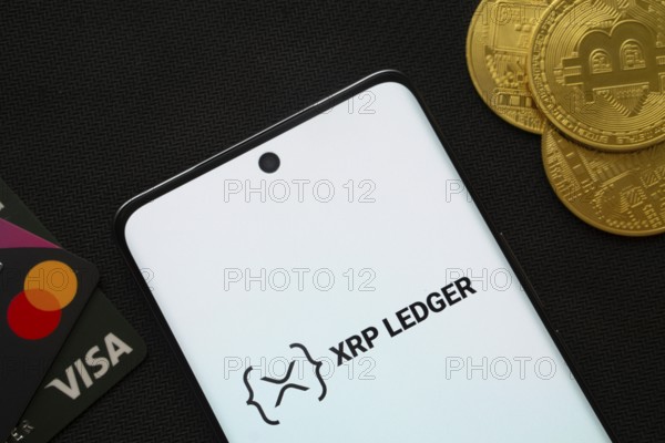 Dhaka, Bangladesh- 26 Aug 2025: Smartphone displaying XRP Ledger logo surrounded by Bitcoin coins and payment cards