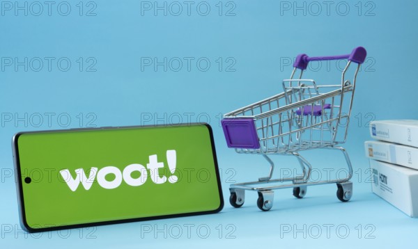 Dhaka, Bangladesh- 03 July 2025: Smartphone with Woot logo next to a small shopping cart and boxes against a blue background