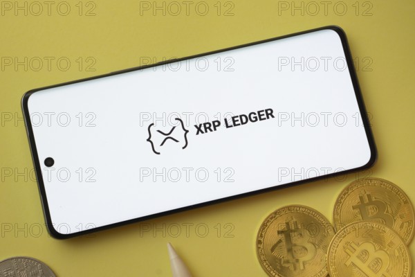 Dhaka, Bangladesh- 26 Aug 2025: XRP Ledger logo on smartphone screen near Bitcoin coin and QR code on background