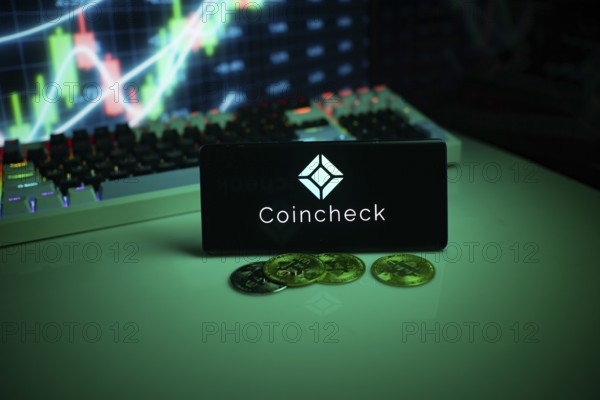 Coincheck on a smartphone with coins and stock market data in the background