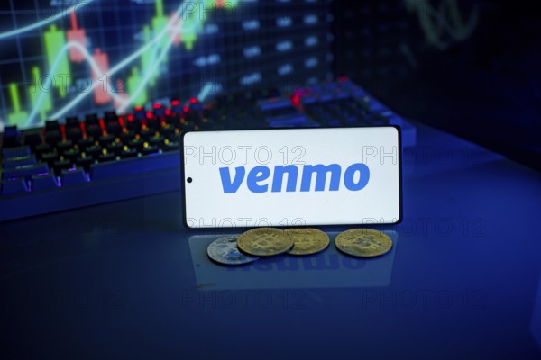 Phone displaying Venmo logo with coins and a backlit keyboard, signifying digital payments and finance