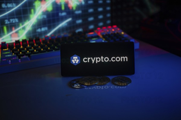 Phone displays Crypto.com logo with crypto coins and vibrant trading screen