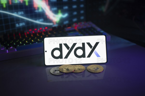 Dydx logo displayed on a phone with digital currencies and trading charts in the background