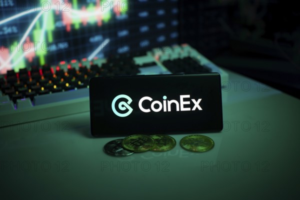 CoinEx logo displayed with coins on a desk and trading graphs in the background
