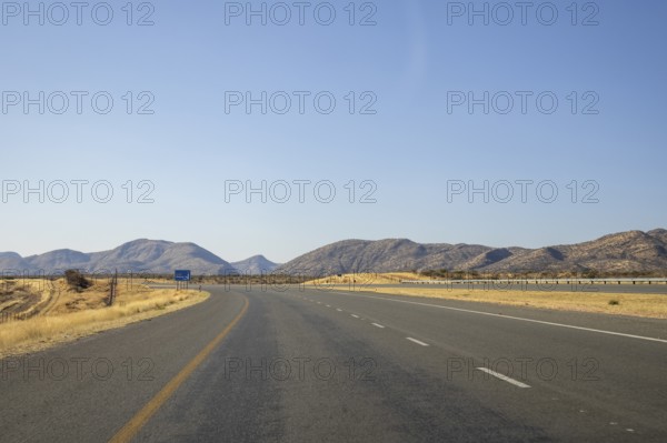 Scenic view of the open road between Windhoek and Outjo, surrounded by dry grasslands and distant mountains under a clear blue sky