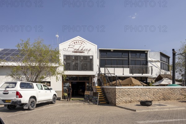 Street view of a modern building with a restaurant or café entrance in Outjo, Namibia 12 Augusto 2025: showing parked cars, outdoor seating, and clear blue sky