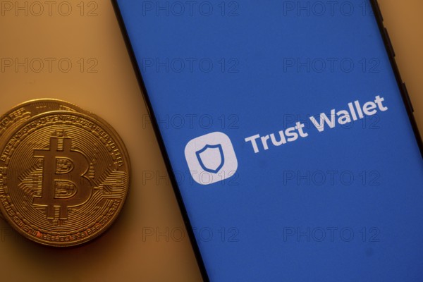 Bitcoin next to a smartphone displaying Trust Wallet app on blue background