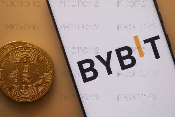 Bitcoin near a smartphone featuring the Bybit logo under orange lighting
