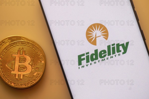 Bitcoin coin next to a smartphone displaying the Fidelity Investments logo on a light background