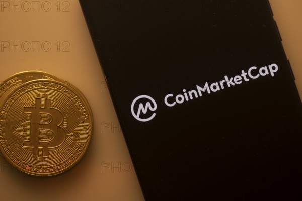 Bitcoin coin beside a phone showing the CoinMarketCap logo on a black screen
