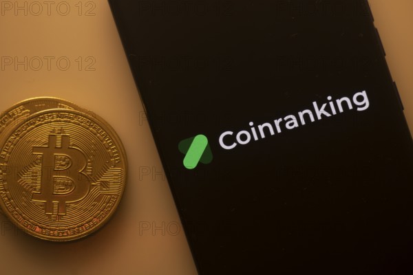 Bitcoin coin beside a phone displaying the Coinranking logo on a black screen