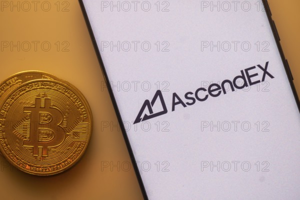 Bitcoin coin next to a smartphone displaying the AscendEX logo on the screen