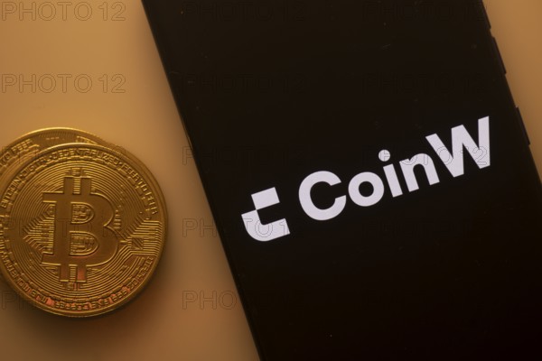CoinW app on mobile screen alongside a Bitcoin coin