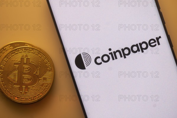Bitcoin next to smartphone with Coinpaper app interface on white background