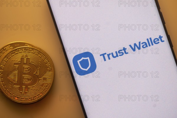 Trust Wallet logo on a smartphone near a Bitcoin coin