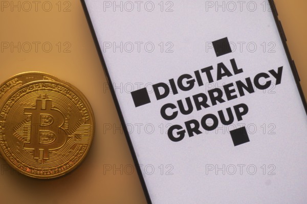 Bitcoin coin next to a smartphone with Digital Currency Group logo on white background