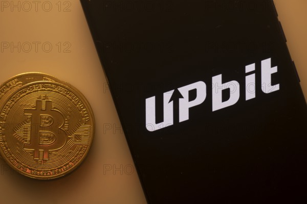 Bitcoin coin beside phone with Upbit logo on black background