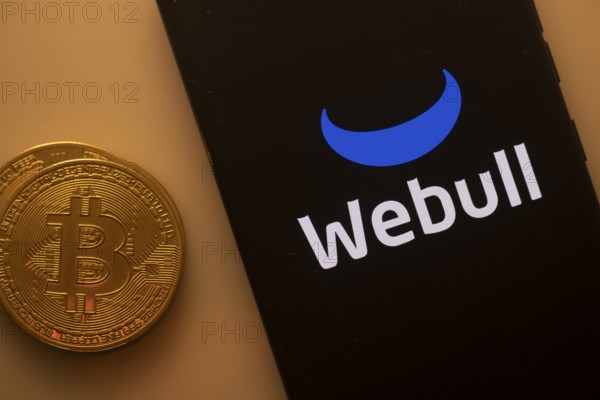 Bitcoin coin next to phone with Webull logo on black background