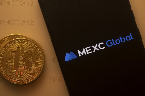 Bitcoin coin beside phone showing MEXC Global logo on a black background
