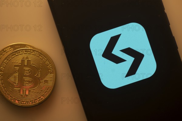 Unidentified logo on smartphone beside Bitcoin, emphasizing cryptocurrency and blockchain technology