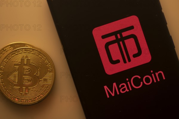 Bitcoin coin beside phone with MaiCoin logo on black background