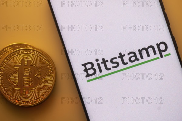 Bitcoin coin next to phone showing Bitstamp logo on white background