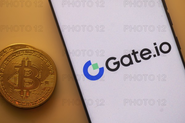 Gate.io logo on a smartphone screen next to a Bitcoin standing on an orange backdrop