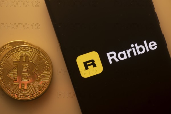 Bitcoin coin beside a phone showing Rarible logo on black screen