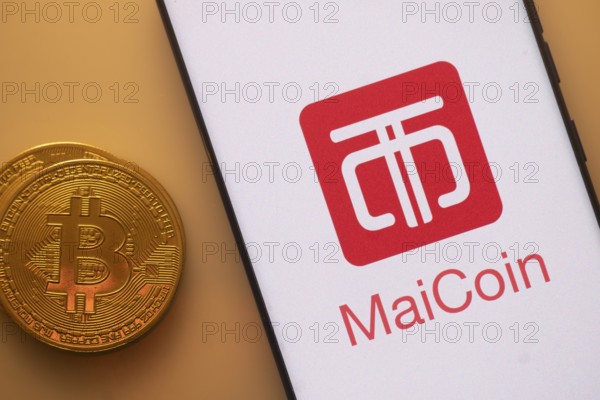 Bitcoin coin beside a phone displaying MaiCoin logo on white screen