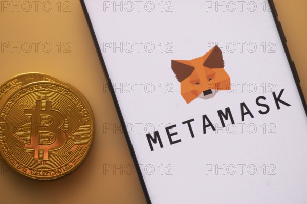 Bitcoin coin alongside a phone showing MetaMask logo on white screen