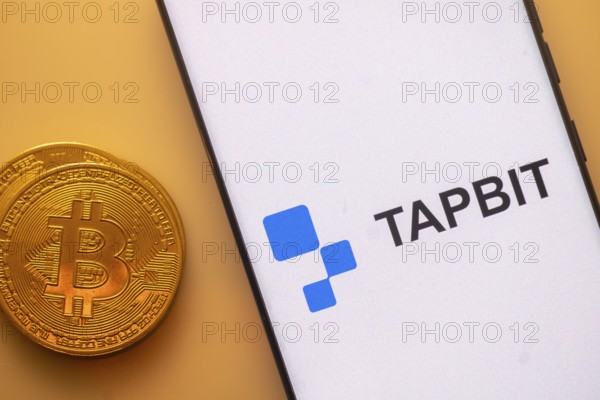 Bitcoin coin beside a phone displaying Tapbit logo on white screen
