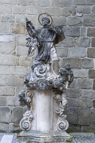 Stone statue of a saint on an ornate pedestal, baroque details in front of a stone wall, parish church St.Stephan Tulln Lower Austria Austria