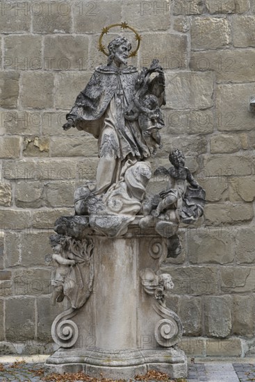 Baroque stone statue of a saint with angel on a decorated pedestal in front of a stone wall, parish church St.Stephan Tulln Lower Austria Austria