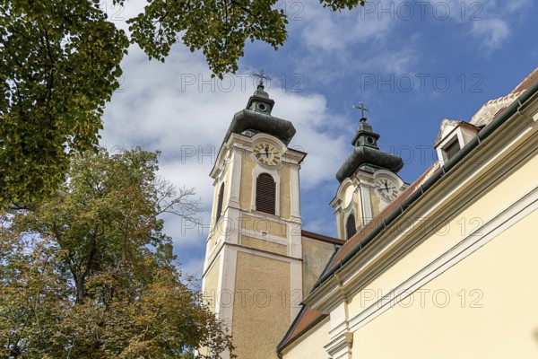 Baroque church towers with clocks in front of a blue sky, surrounded by autumnal trees, parish church St.Stephan Tulln Lower Austria Austria