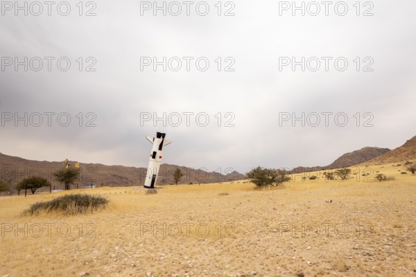 A mock Soviet rocket stands nose-first in the Solitaire, Namibian desert, surrounded by golden grasslands and rugged mountains under cloudy skies
