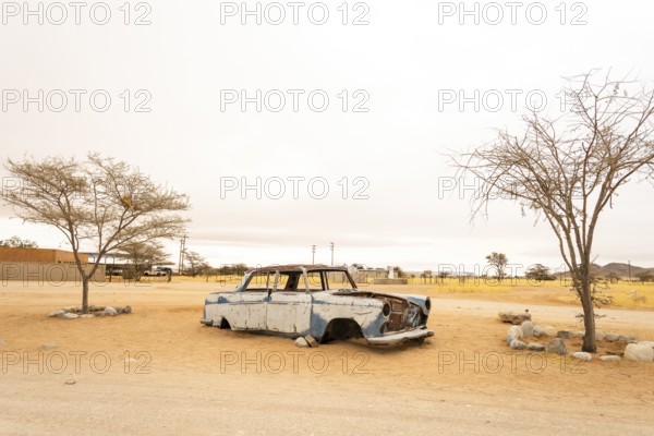 Solitaire's car graveyard in Namibia features rusted vintage cars near small desert buildings, set against dunes and mountains, capturing desert charm and isolation