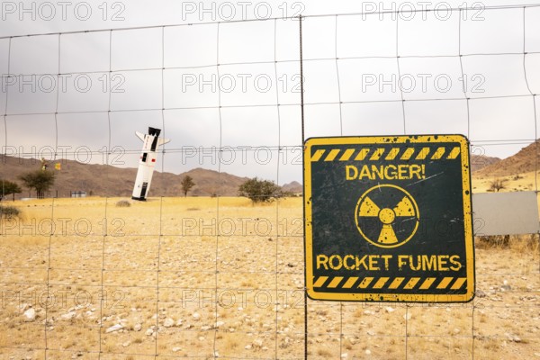 A mock Soviet rocket stands nose-first in the Solitaire, Namibian desert, surrounded by golden grasslands and rugged mountains under cloudy skies
