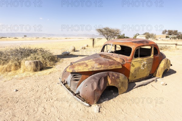 Solitaire's car graveyard in Namibia features rusted vintage cars near small desert buildings, set against dunes and mountains, capturing desert charm and isolation