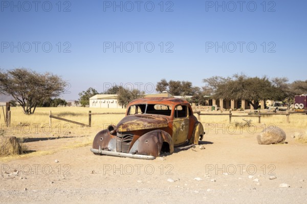 Solitaire's car graveyard in Namibia features rusted vintage cars near small desert buildings, set against dunes and mountains, capturing desert charm and isolation