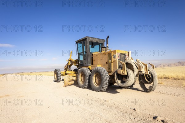 In the remote desert near Solitaire, Namibia, a tractor levels a dirt road across golden sand dunes and rugged desert terrain