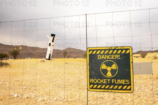 A mock Soviet rocket stands nose-first in the Solitaire, Namibian desert, surrounded by golden grasslands and rugged mountains under cloudy skies