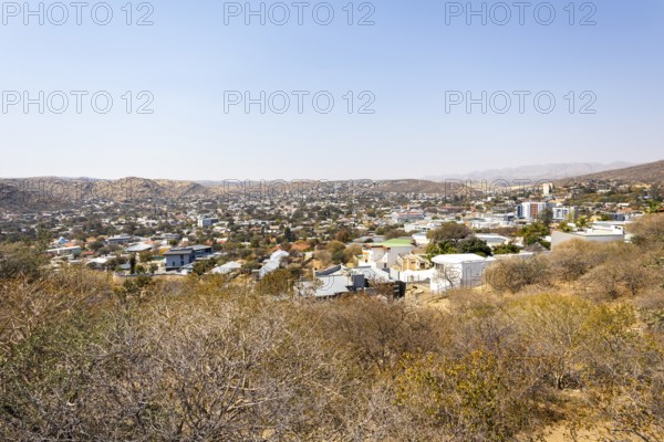 A panoramic view of Windhoek, Namibia, from the National Botanic Garden, showing the city's mix of homes, modern buildings, and a distant church framed by dry hills and mountains
