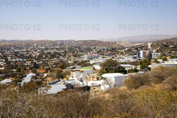 A panoramic view of Windhoek, Namibia, from the National Botanic Garden, showing the city's mix of homes, modern buildings, and a distant church framed by dry hills and mountains